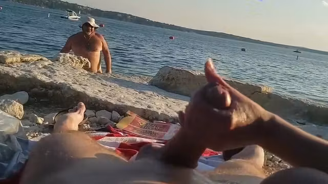 On a nude beach the wife stokes my cock while a voyuer watches